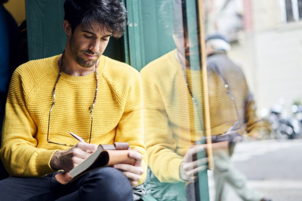 A man wearing a yellow sweater writing in a notepad