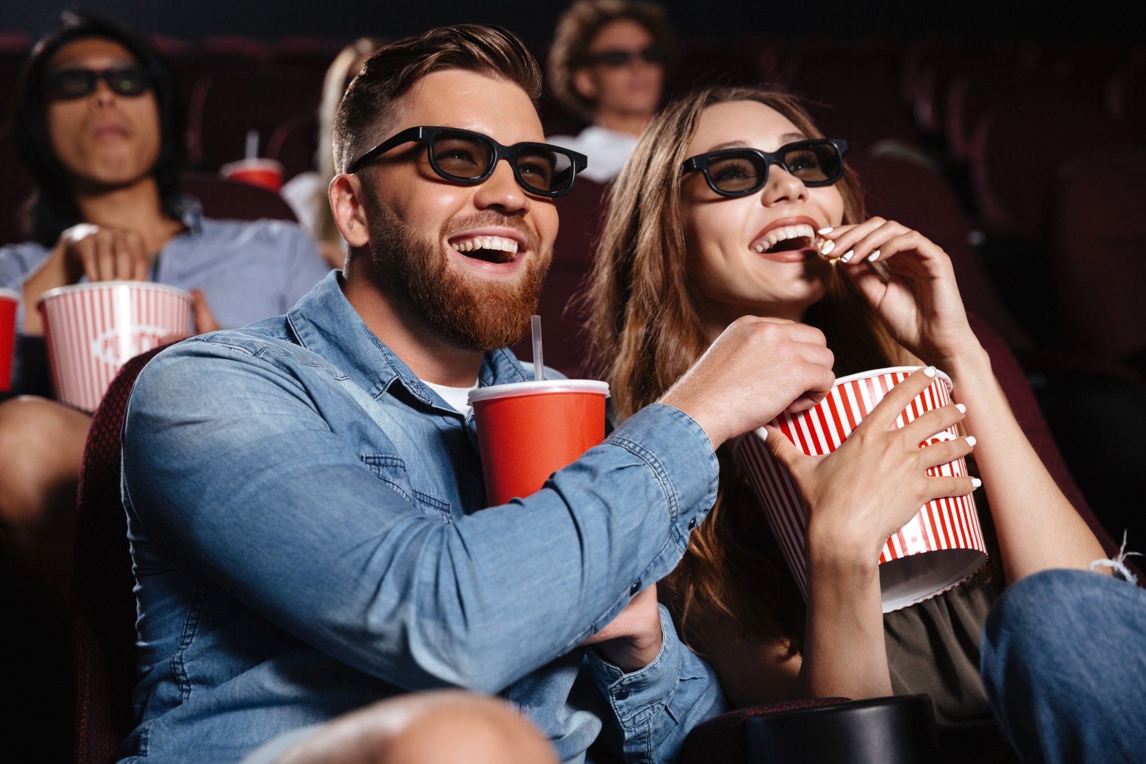 Friends sitting in the theater watch a film and eating popcorn